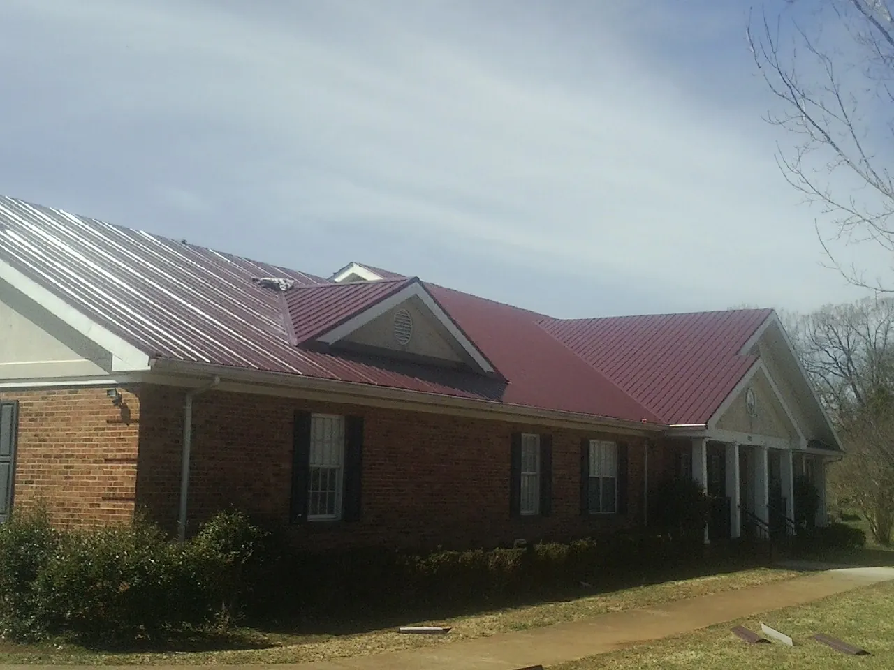 Red metal roof with gabled entries on a long brick building, from a Hail Damage Roof Repair job in Ray City