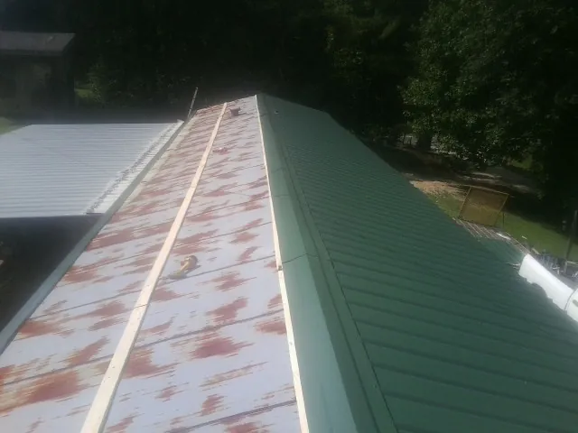Old rusted panels beside newly installed green metal roofing — Wind Damage Roof Repair by Roofing Brothers in Ray City