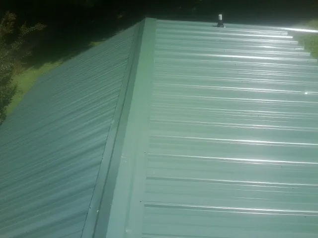 New green metal panels meeting at the ridge of a roof — Flat Roof Repair work by our crew in Ray City