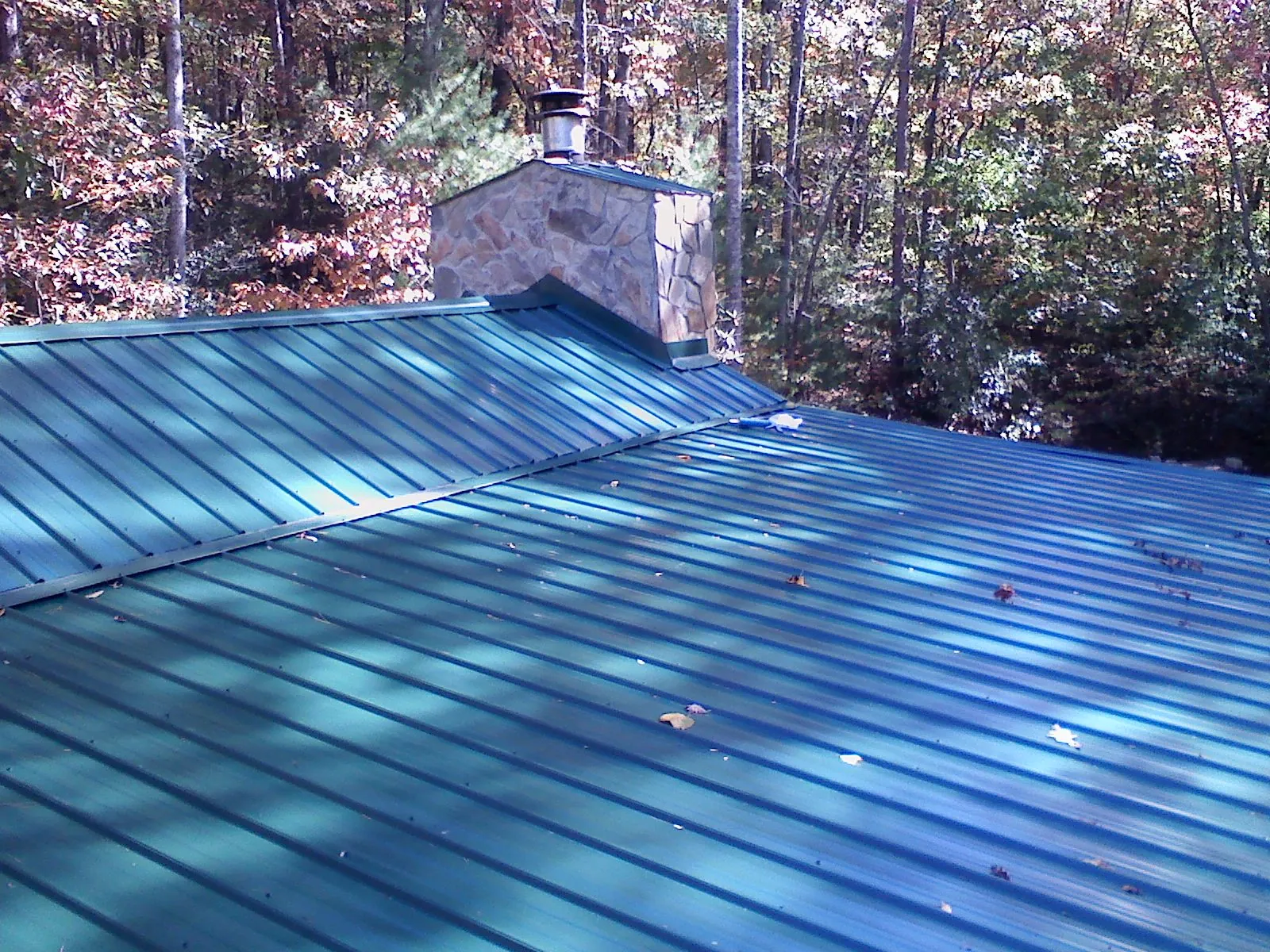 New green metal roof and stone chimney surrounded by autumn woods in Ray City