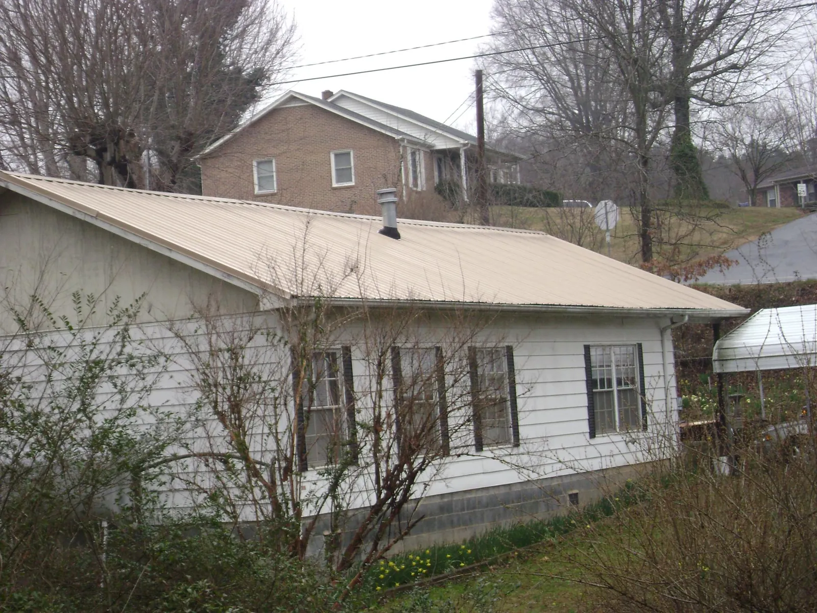 Tan metal roof on a white sided house set into a hillside — Commercial Roofing by Roofing Brothers in Ray City